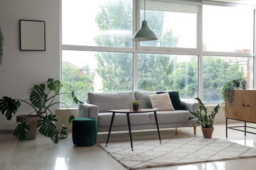 Interior of modern living room with cozy grey sofa near big window