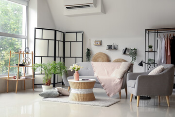 Interior of light living room with comfortable grey sofa, armchair and coffee table