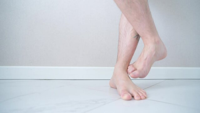 Close-up of men's feet barefoot on a tiled floor. Man walking on tiled white floor.