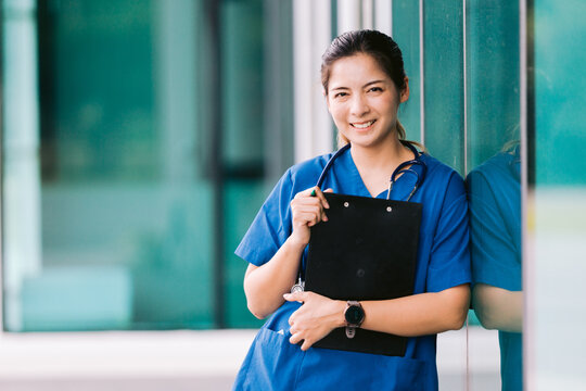 Portrait of young Asian female doctor writing on clipboard in hospital corridor