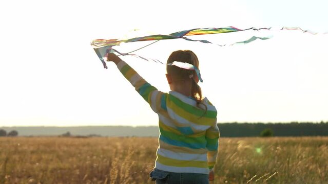 little girl with flying kite plays sunset. happy child family. kid daughter park plays with a flying kite glare sunlight. child walks with children toy. flying kite soars wind. happy child dream fly.