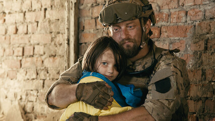 A soldier in a Ukrainian military uniform hugs his little girl with the Ukrainian flag. The concept...