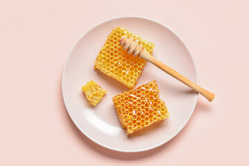 Plate with sweet honeycombs and dipper on pink background