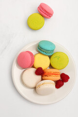 Plate with sweet macaroons and raspberries on white background
