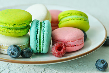 Plate with sweet macaroons and berries on light blue background