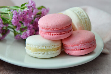 Plate with sweet macaroons and beautiful flowers on pink background