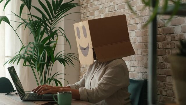 One modern worker wearing carton box on his head to protect privacy. Concept of online alignment job. Employees smiling at the desk in home office small business indoor activity. Surfing the web vpn