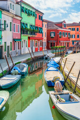 Picturesque colorful idyllic scene with a boats docked on the water canals in Burano Venice Italy. Water reflection.