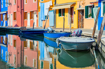 Fototapeta na wymiar Picturesque colorful idyllic scene with a boats docked on the water canals in Burano Venice Italy. Water reflection.