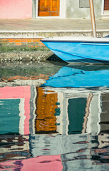 Picturesque colorful idyllic scene with a boat docked on the water canals in Burano Venice Italy. Water reflection.