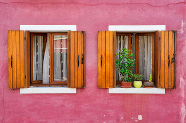 Detail with a colorful house windows with lots of flower pots and wooden shutters in Burano, Italy.