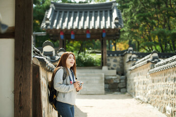 A young woman wearing a camera and taking pictures while traveling to tourist attractions with traditional Korean houses