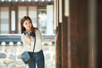Fototapeta premium A young woman wearing a camera and taking pictures while traveling to tourist attractions with traditional Korean houses