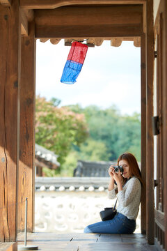 A young woman wearing a camera and taking pictures while traveling to tourist attractions with traditional Korean houses
