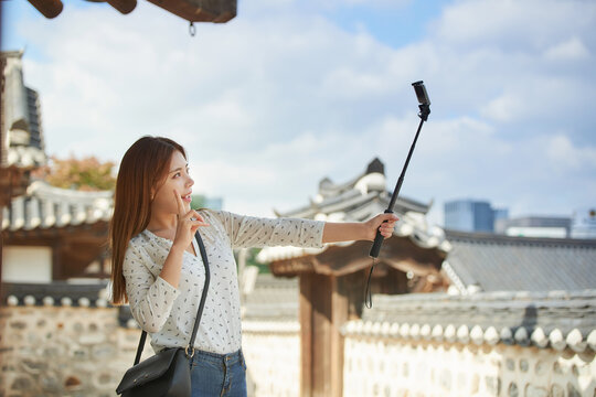 A young woman who is taking pictures with a smartphone camera while traveling in a traditional Korean village