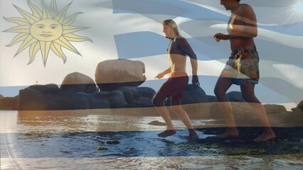 Animation of waving uruguay flag over group of diverse friends running and having fun at the beach - Powered by Adobe