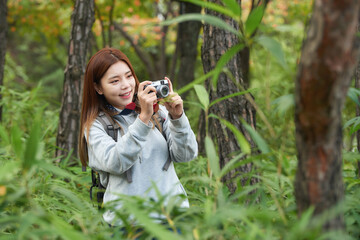 A young woman walking around in the woods taking pictures with a camera and backpack