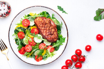 Salad with grilled duck breast and cherry tomatoes, cucumber, paprika, lettuce and arugula on white table background, top view