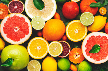 Colorful citrus fruis, food background, top view. Mix of different whole and sliced fruits: orange, grapefruit, lemon, lime and other with leaves on  green stone table - obrazy, fototapety, plakaty
