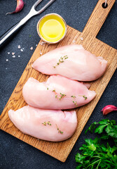 Raw chicken breast fillet on rustic cutting board prepared for cooking with garlic, thyme, spices...