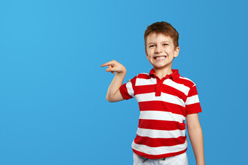 Excited cute little kid boy in red striped polo shirt pointing to empty space on background