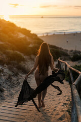 Chica de espaldas con pelo largo bajando por pasarela de madera a playa paradisiaca al atardecer 