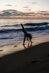 Silueta de chica realizando movimientos de gimnasia y baile al atardecer en playa paradisiaca