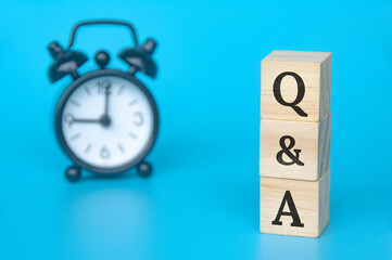 Q and A text on wooden blocks with light blue and alarm clock background. Question and answer concept. Copy space