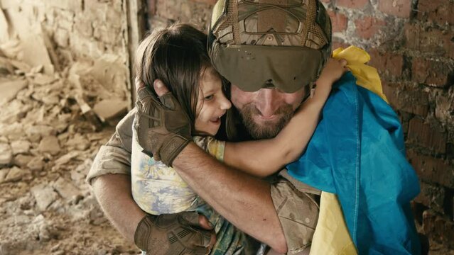A soldier in a Ukrainian military uniform hugs his little girl with the Ukrainian flag. The concept of saving children from war