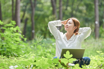 A young woman is using a laptop in a forested park.