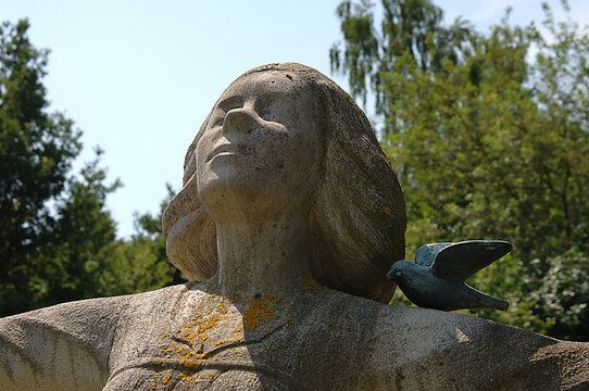 Statue eines Mädchen mit Taube auf der Schulter auf einem Friedhof