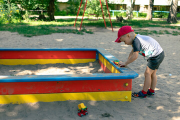 A child plays with a small train on the sandbox. Small boy plays next to a wooden sandbox