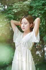 In summer daytime, a beautiful Asian woman wearing a dress in a forested park is doing various movements.