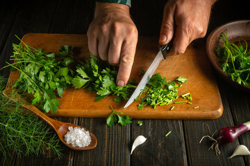 Close-up of a cook hands cutting fresh parsley on a cutting board with a knife. work environment with vegetables on the kitchen table. The idea of a vegetarian or vegetable diet