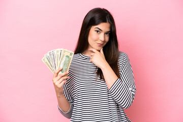Young Brazilian woman taking a lot of money isolated on pink background thinking