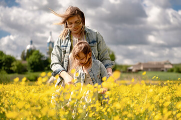 Young mother and daughter spend time together in a field with yellow flowers, family, love