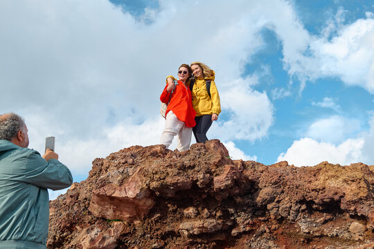 Hiking on tallest volcano in Continental Europe - Etna. Group of friends taking photo on the mountain peak of panoramic view of Mount Etna with cloudy sky in background.