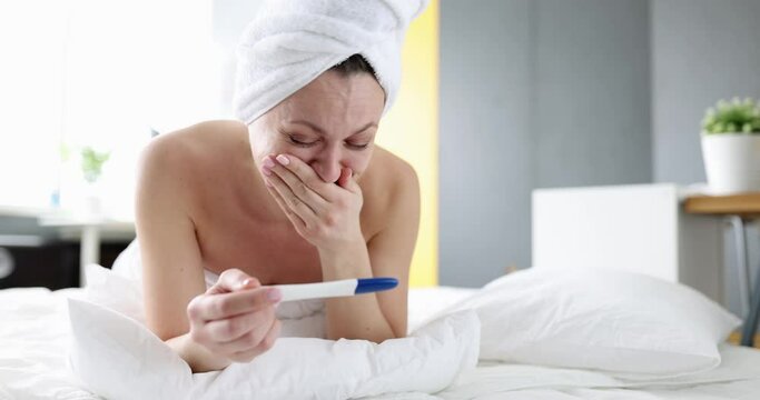A woman lying on a bed rejoices at a pregnancy test, close-up. Joy of motherhood, positive test result