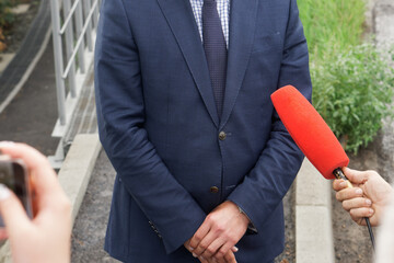 An official man in a jacket gives an interview to reporters on the street. Red microphone and...