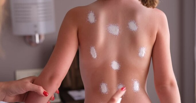Mom in the room applies sunscreen to the child's back, close-up. Protecting baby skin in summer, sunbathing
