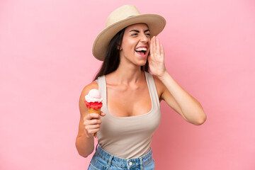 Young caucasian woman with a cornet ice cream isolated on pink background shouting with mouth wide...