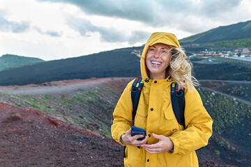 Hiking on tallest volcano in Continental Europe - Etna. Young smiling woman in yellow raincoat in...