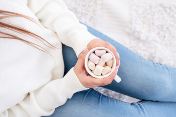 Woman in warm white winter sweater holding cup with marshmallows