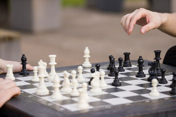 Closeup of a man's at a table and plays chess. The teenager picked up the chess piece and makes his...