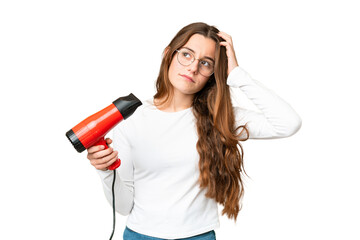 Teenager girl holding a hairdryer over isolated chroma key background having doubts and with confuse face expression