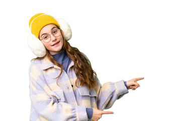 Teenager girl wearing winter muffs over isolated chroma key background pointing finger to the side and presenting a product
