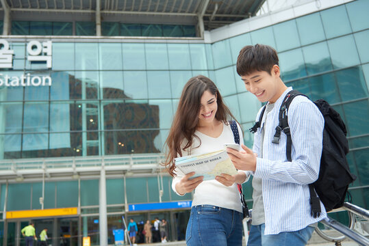  A couple dragging suitcases and looking at a map at a Korean train station