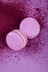 Obraz na płótnie Canvas Pastel colored sweet french macaroons and splash of dry blueberry powder on purple background. Beautiful composition for bakery and pastry shop, top view