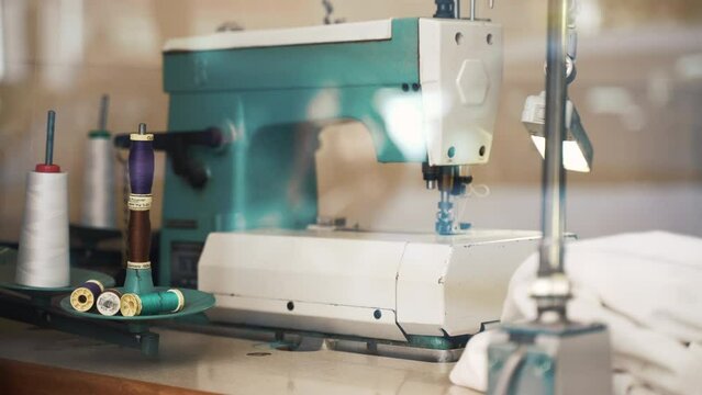 Retro style tailor's workshop, vintage sewing machine, fabric thread spools, needles, pins, shears, chalk and tape measure for working process, sewing tool, equipments and details reflecting in