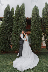 Fototapeta premium A beautiful wedding, a beautiful couple in love, laughing and kissing against the background of a green garden. High quality photo